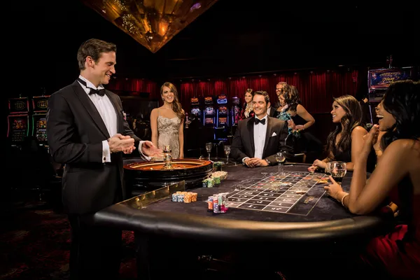 Um dealer profissional de smoking cumprimentando jogadores na mesa de roleta, simbolizando a autêntica sensação de cassino ao vivo no 777AN.